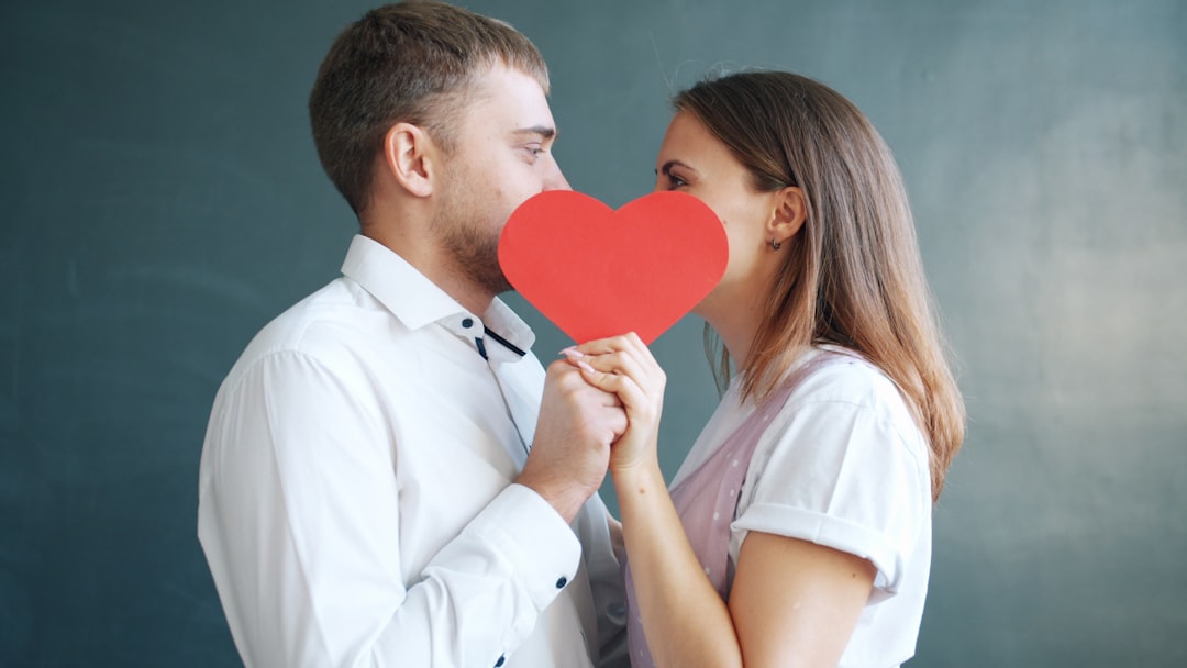 Beautiful young couple man and woman are kissing hiding behind Valentines card on gray background. Human feelings, millennials and celebrations concept.